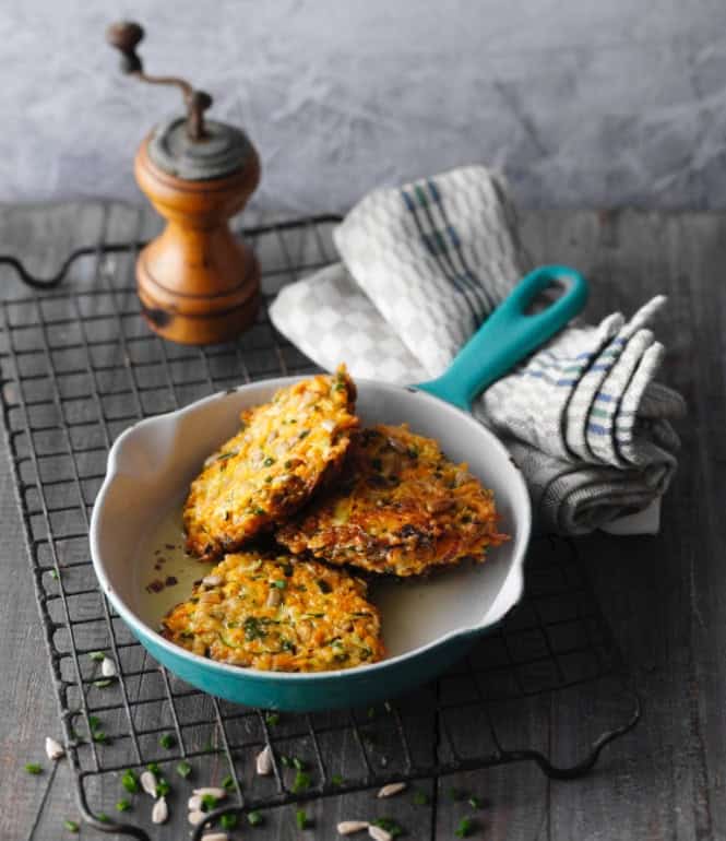 Knusprige Möhren-Zucchini-Puffer in einer Pfanne mit Sonnenblumenkernen, serviert auf einem Drahtgitter.
