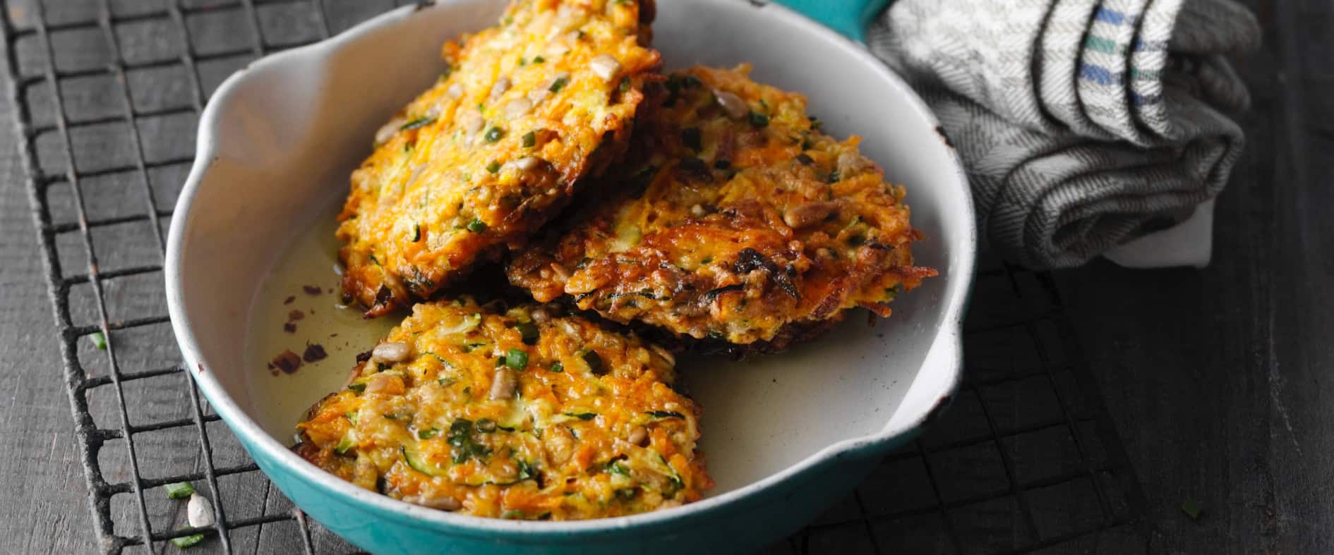 Knusprige Möhren-Zucchini-Puffer in einer Pfanne mit Sonnenblumenkernen, serviert auf einem Drahtgitter.