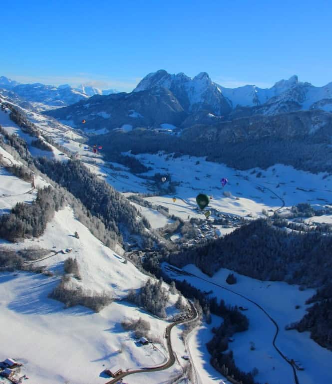 Heißluftballons schweben über dem verschneiten Château-d’Oex im Schweizer Waadtland.