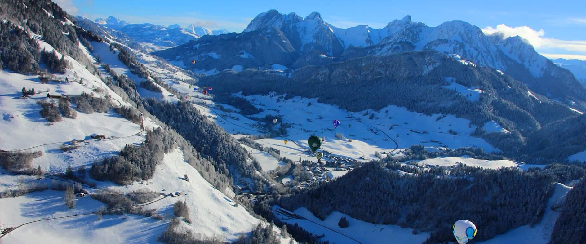 Heißluftballons schweben über dem verschneiten Château-d’Oex im Schweizer Waadtland.