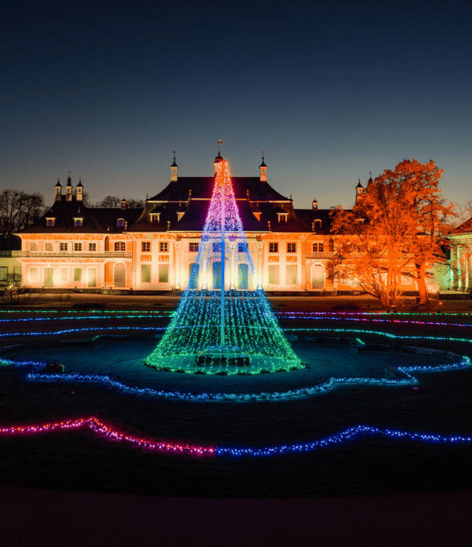 Beleuchteter Schlossgarten von Schloss & Park Pillnitz mit farbigen Lichtinstallationen beim Christmas Garden Dresden in der Abenddämmerung.