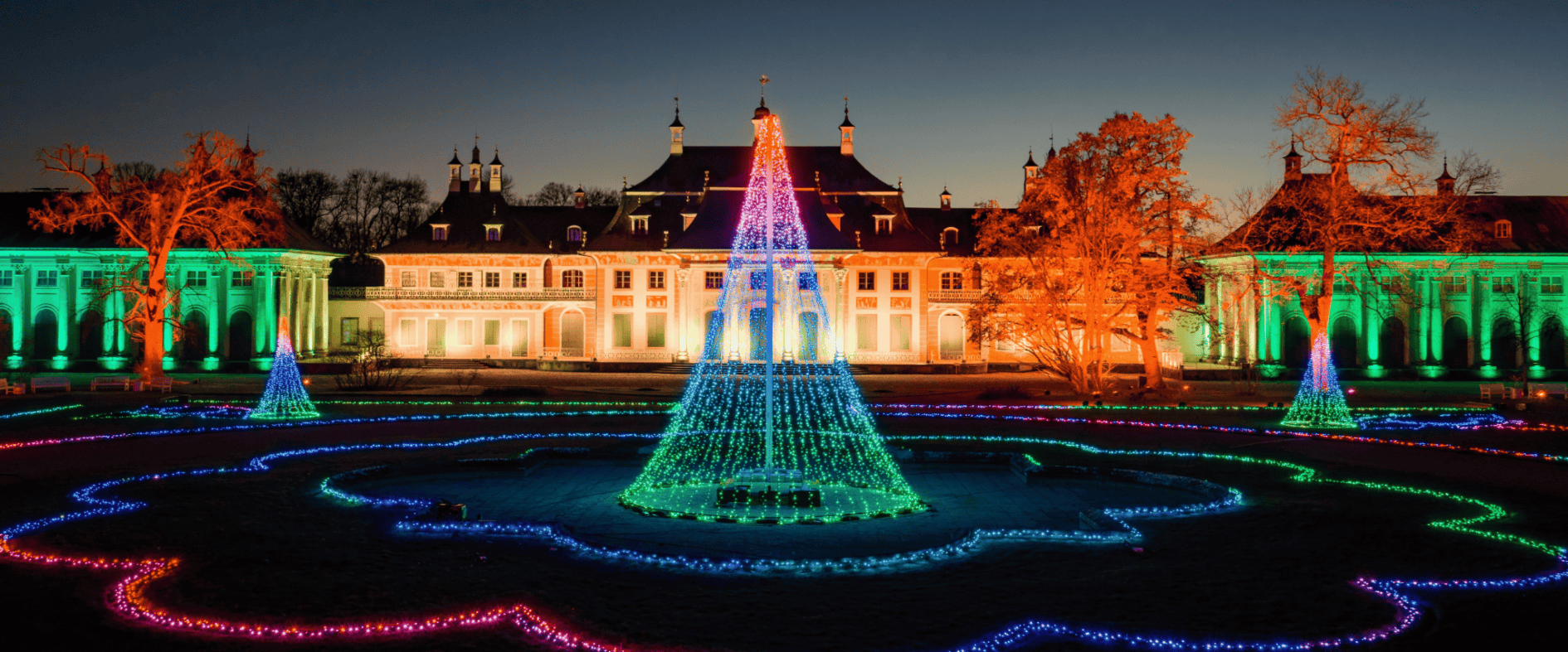 Beleuchteter Schlossgarten von Schloss & Park Pillnitz mit farbigen Lichtinstallationen beim Christmas Garden Dresden in der Abenddämmerung.