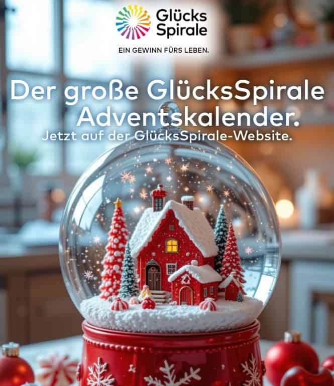 Der große GlücksSpirale Adventskalender – Schneekugel mit rotem Haus und Weihnachtsbaum, im Hintergrund festlich dekorierte Küche