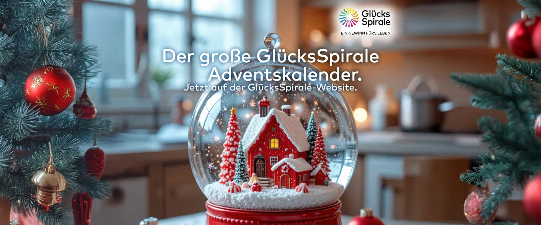 Der große GlücksSpirale Adventskalender – Schneekugel mit rotem Haus und Weihnachtsbaum, im Hintergrund festlich dekorierte Küche