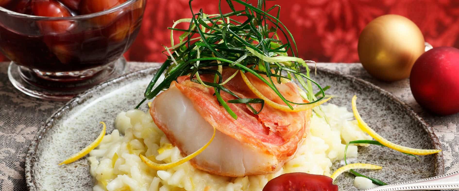 Kabeljau-Saltimbocca im Pancetta-Mantel auf cremigem Lauchrisotto, garniert mit frittiertem Lauch und Zitronenzesten, dazu Portweinfeigen auf einem festlich angerichteten Teller.