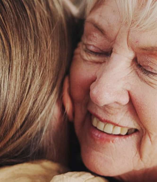 Ältere Frau umarmt ein Familienmitglied und lächelt – symbolische Darstellung von geteilter Freude und Dankbarkeit.
