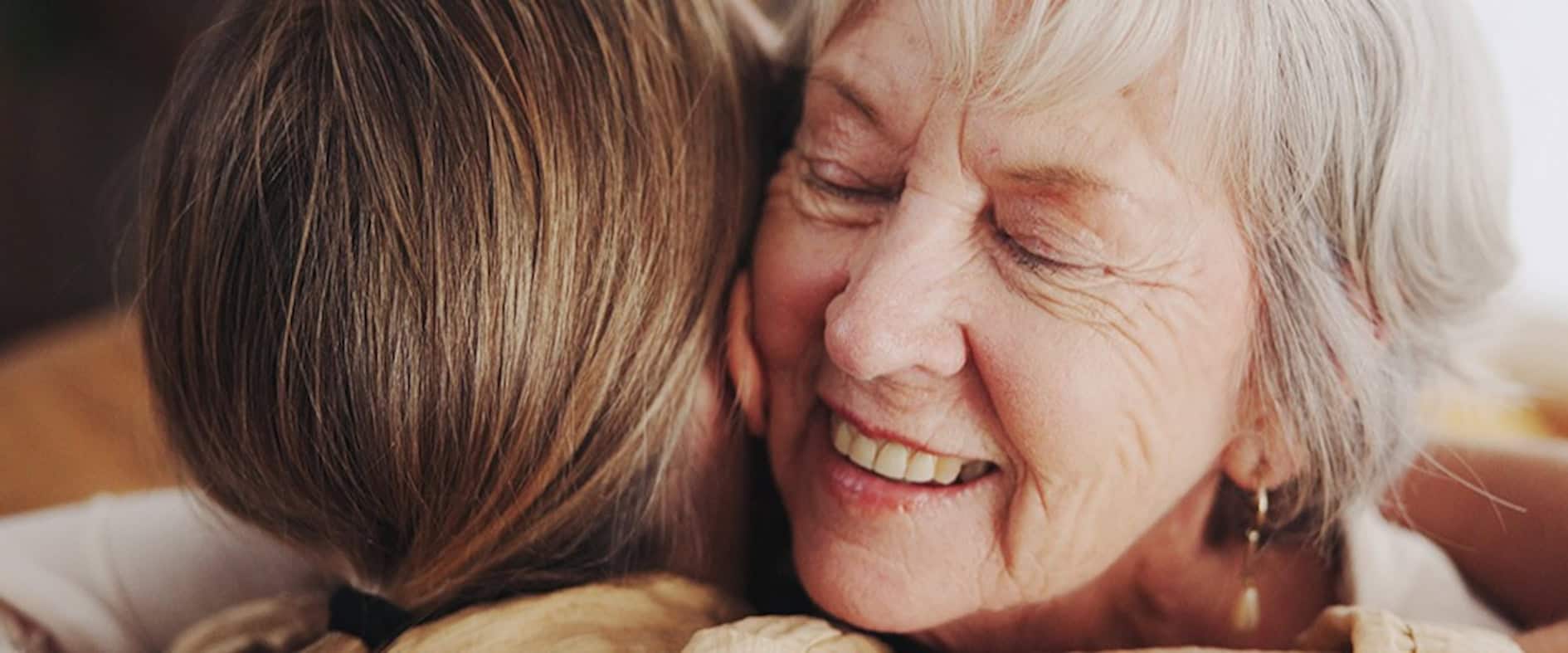 Ältere Frau umarmt ein Familienmitglied und lächelt – symbolische Darstellung von geteilter Freude und Dankbarkeit.