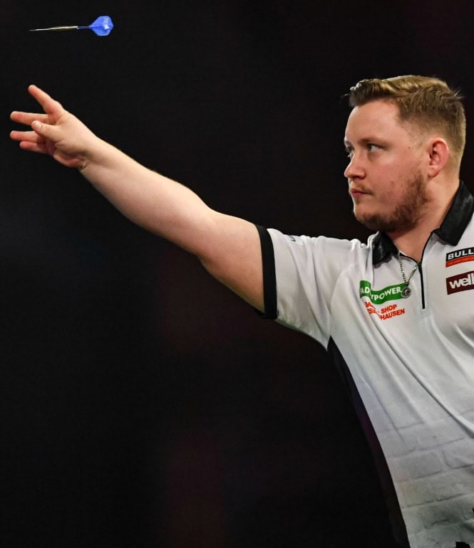 Dartspieler Martin Schindler wirft einen Pfeil präzise in Richtung Scheibe, fokussiert und in Wettkampfatmosphäre.