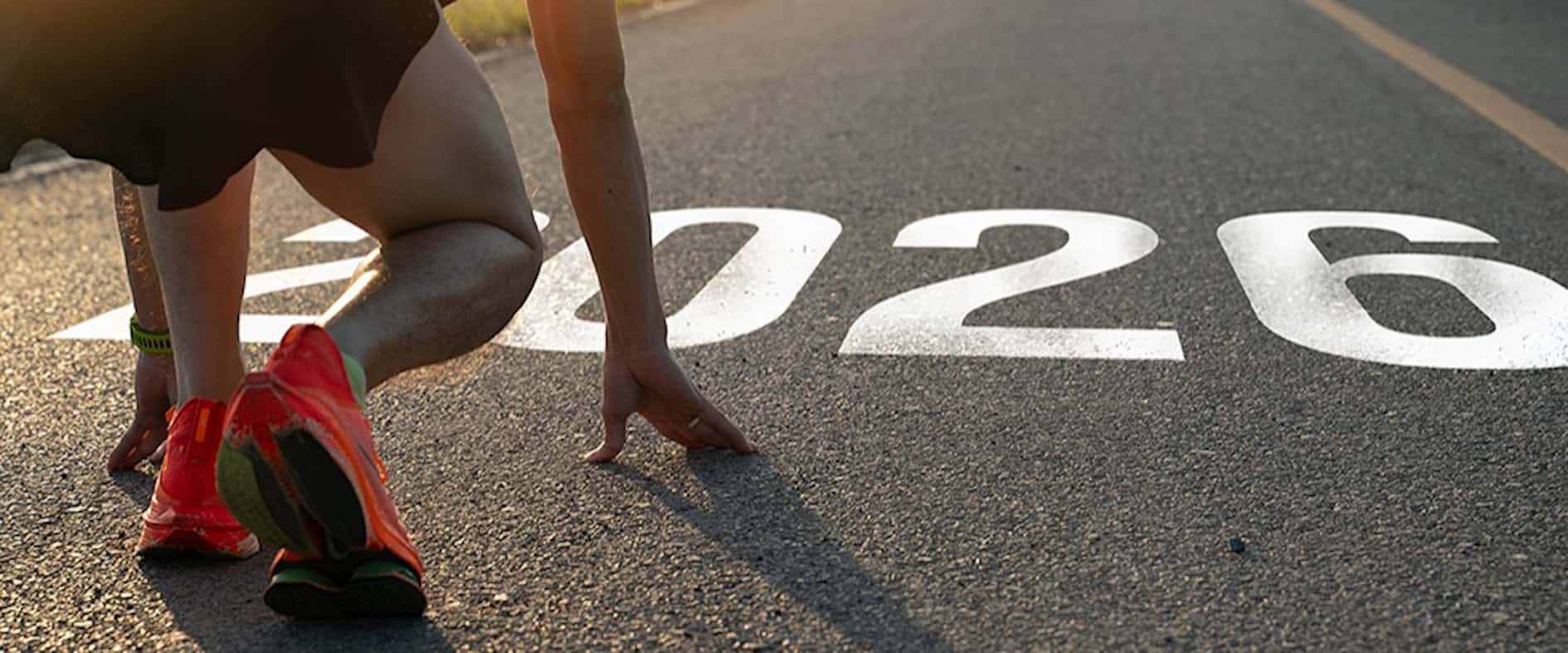 Athlet in Startposition auf einer Straße mit der Jahreszahl 2026 auf dem Asphalt.