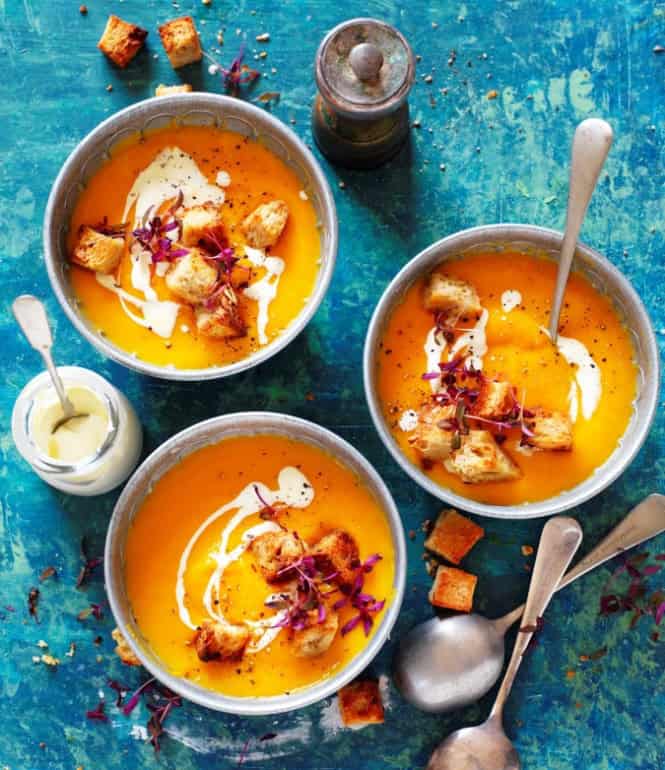 Cremige Süßkartoffel-Kürbis-Suppe in drei Schalen, serviert mit knusprigen Toast-Croutons, einem Klecks Saurer Sahne und frischen Kräutern.