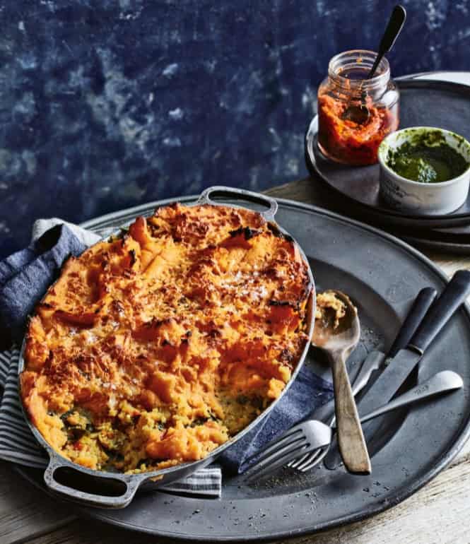 Vegetarischer Shepherd’s Pie aus Kartoffeln, Süßkartoffeln und Gemüse-Reis, goldbraun überbacken in einer Ofenform, serviert rustikal mit Besteck und Pesto.