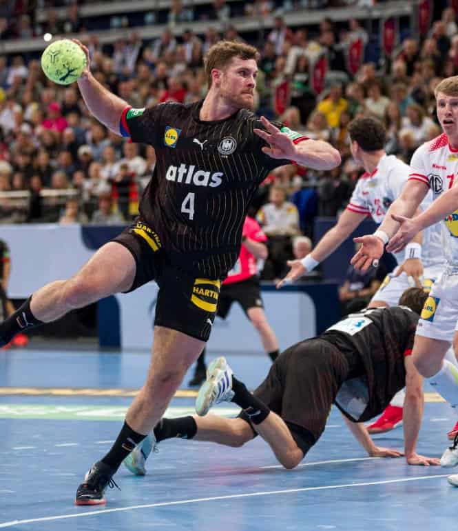 Handballspieler der deutschen Nationalmannschaft springt zum Wurf im Spiel gegen ein gegnerisches Team vor voller Arena.