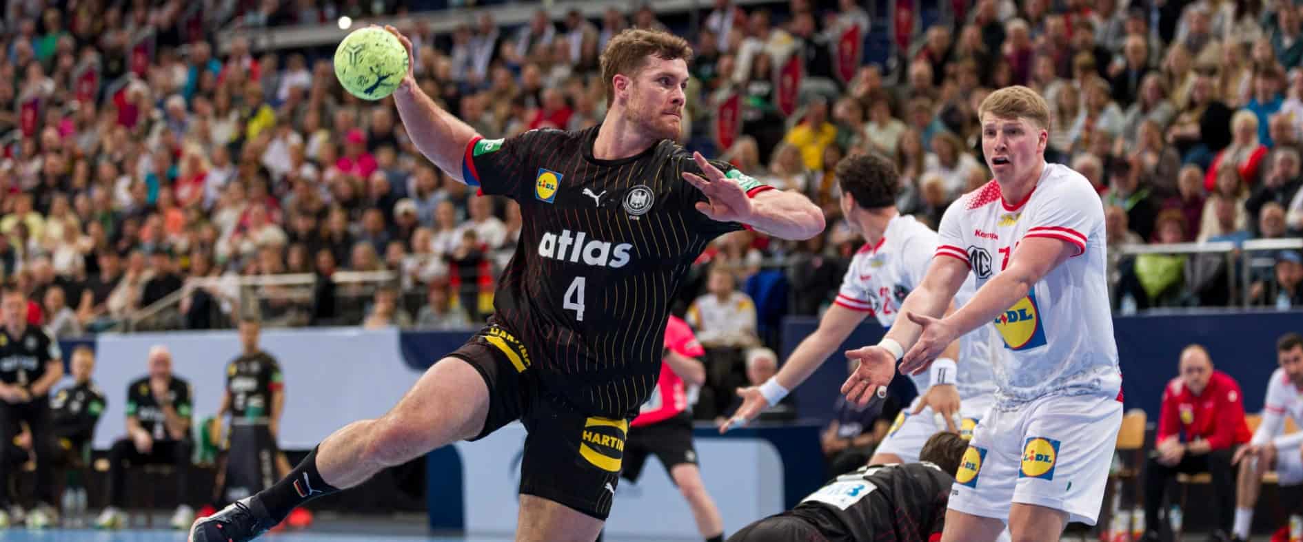 Handballspieler der deutschen Nationalmannschaft springt zum Wurf im Spiel gegen ein gegnerisches Team vor voller Arena.