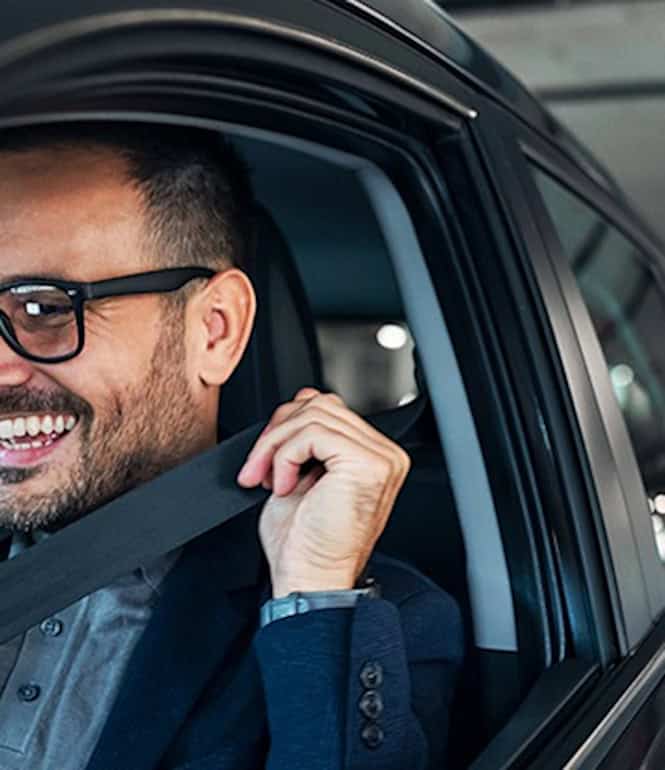 Lächelnder Mann im Anzug sitzt glücklich in seinem Auto auf einem Parkplatz und freut sich über einen freien Parkplatz – manchmal führen kleine Glücksmomente zu großen Chancen.