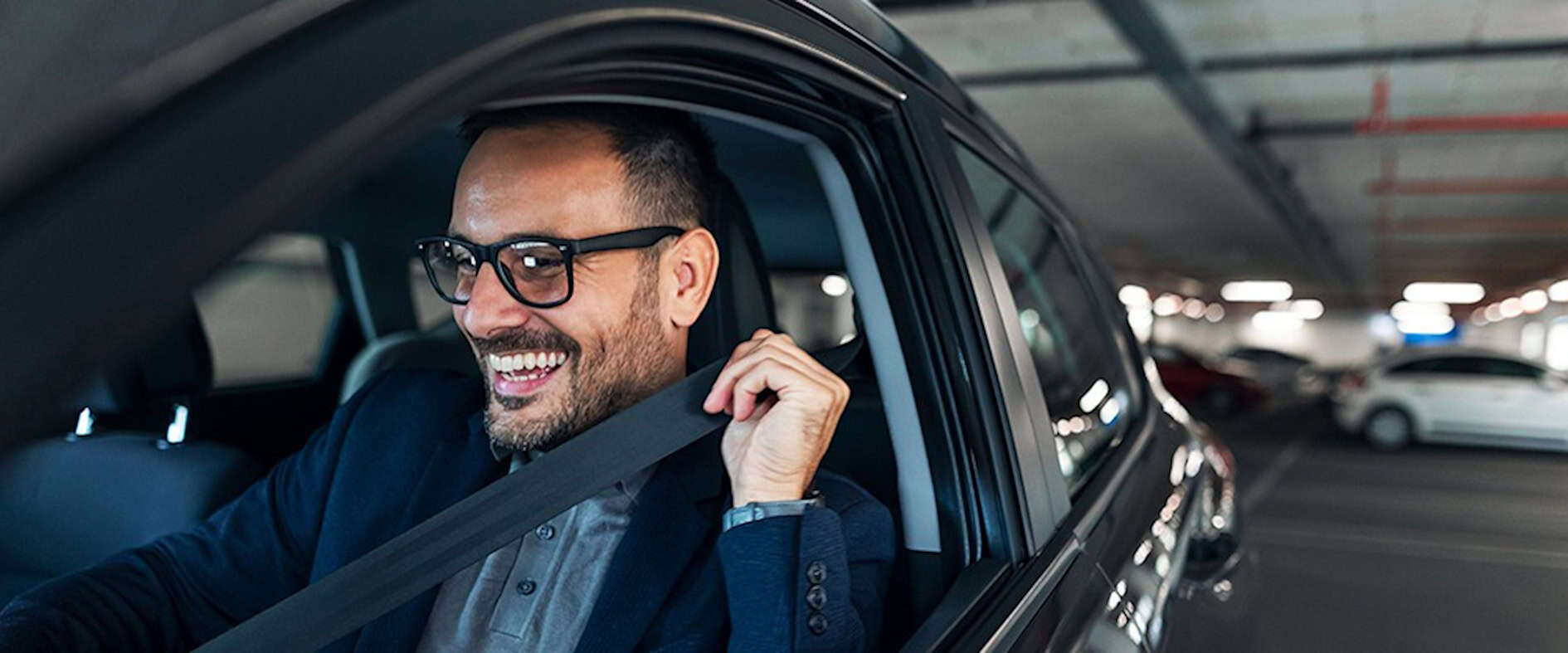 Lächelnder Mann im Anzug sitzt glücklich in seinem Auto auf einem Parkplatz und freut sich über einen freien Parkplatz – manchmal führen kleine Glücksmomente zu großen Chancen.