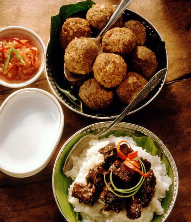 Indonesische Hackbällchen und geschmortes Rindfleisch in dunkler Sojasauce, serviert mit weißem Reis und Tomaten-Chili-Dip in kleinen Schalen.