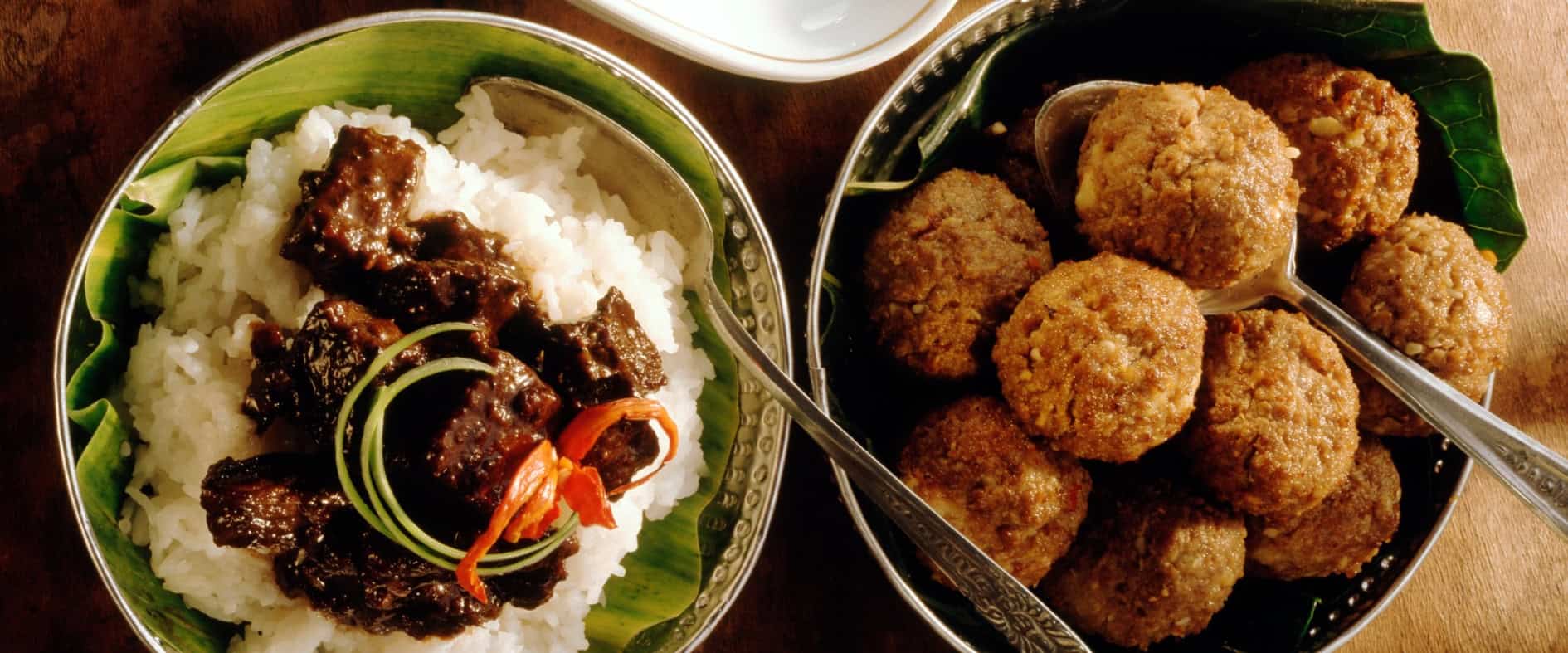 Indonesische Hackbällchen und geschmortes Rindfleisch in dunkler Sojasauce, serviert mit weißem Reis und Tomaten-Chili-Dip in kleinen Schalen.