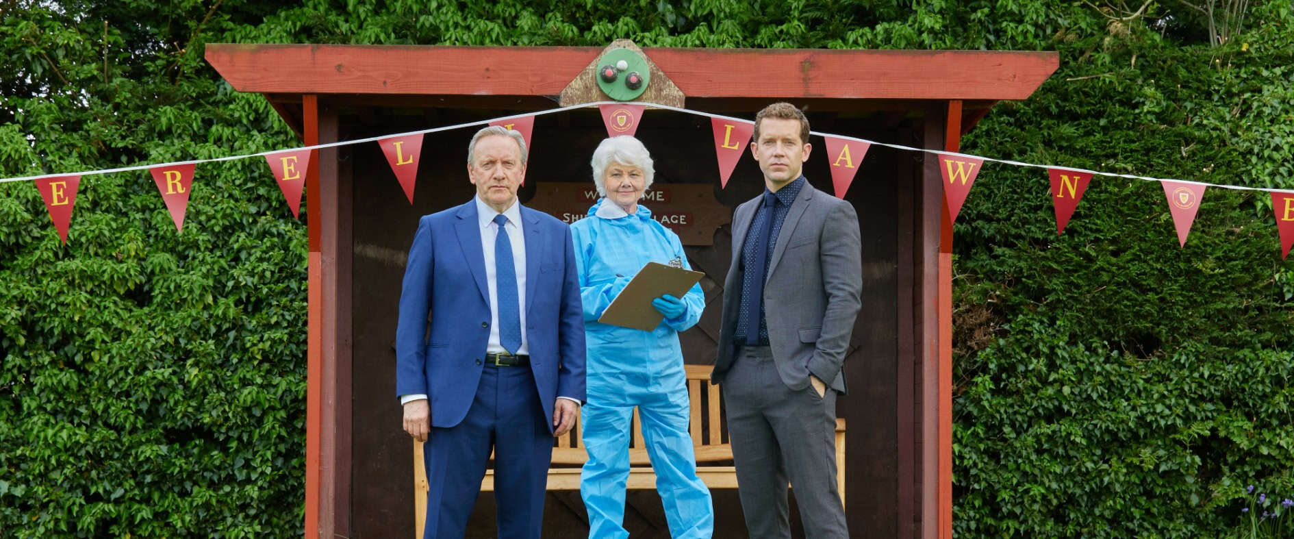 Drei Ermittler stehen auf einem Bowling Green vor einem Vereinsunterstand mit Wimpelkette, bereit zur Untersuchung eines Mordfalls.