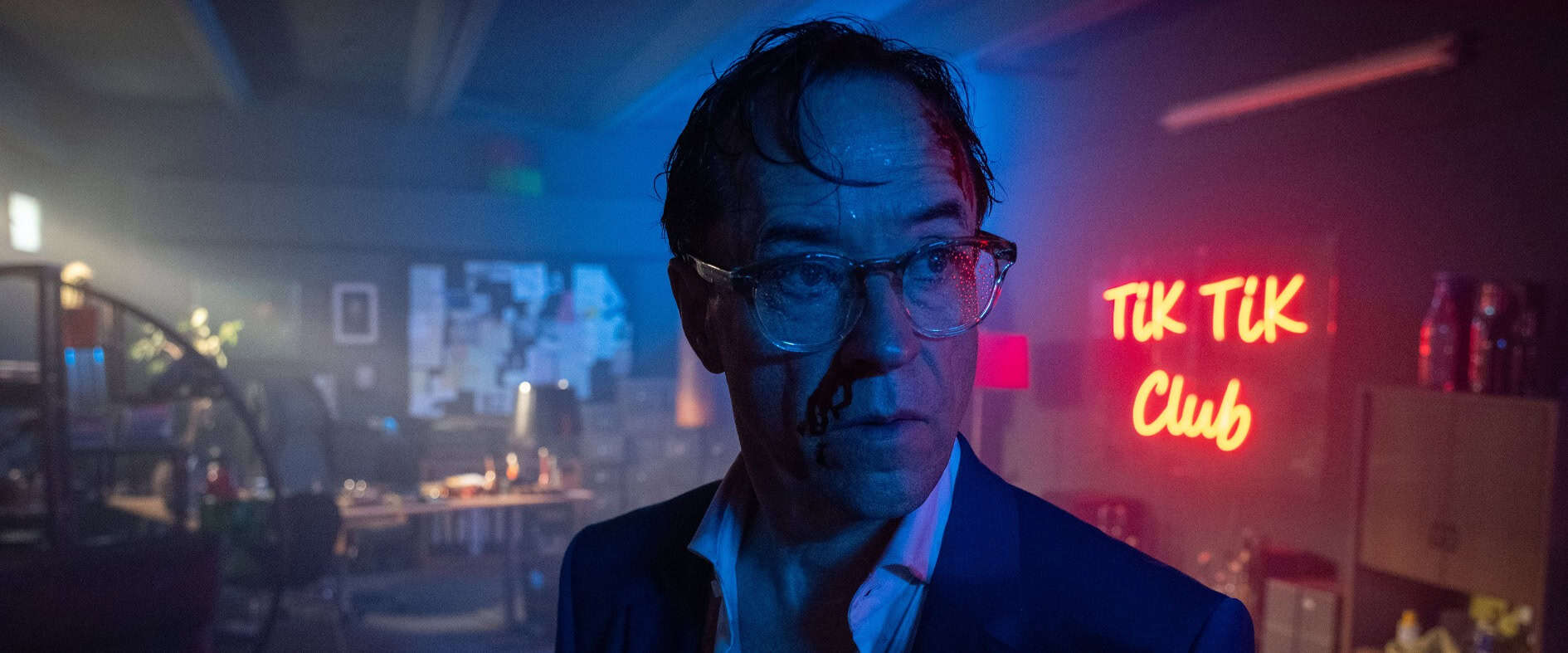 Jan Josef Liefers als Anwalt Joachim Vernau in einer düsteren Szene des Thrillers 'Der schwarze Schwan' – im Hintergrund leuchtet das Neon-Schild 'TIK TIK Club'.