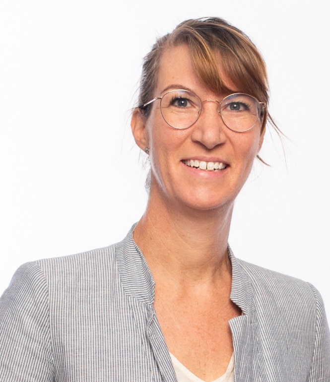 Prof. Susanne Kobel, lächelnd vor hellem Hintergrund, mit Brille und hell gestreifter Jacke.