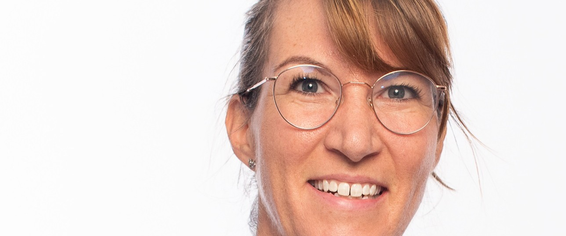 Prof. Susanne Kobel, lächelnd vor hellem Hintergrund, mit Brille und hell gestreifter Jacke.