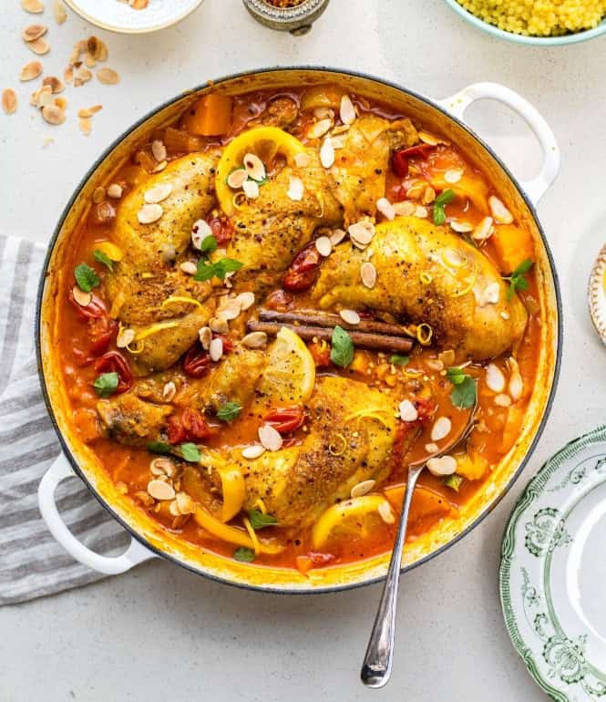 Marokkanische Hähnchen-Tajine mit Kürbis, Kirschtomaten und Aprikosen in würziger Sauce, garniert mit Mandeln, Minze und Zitronenscheiben.