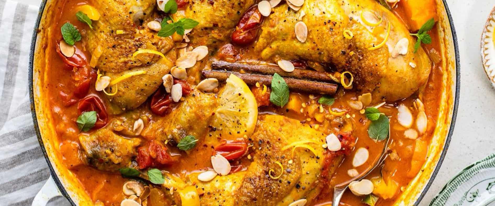 Marokkanische Hähnchen-Tajine mit Kürbis, Kirschtomaten und Aprikosen in würziger Sauce, garniert mit Mandeln, Minze und Zitronenscheiben.