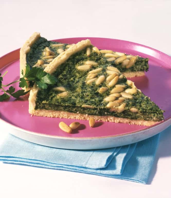 Zwei Stücke Spinatquiche mit Pinienkernen auf knusprigem Mürbeteig, serviert auf einem Teller und mit Petersilie garniert.