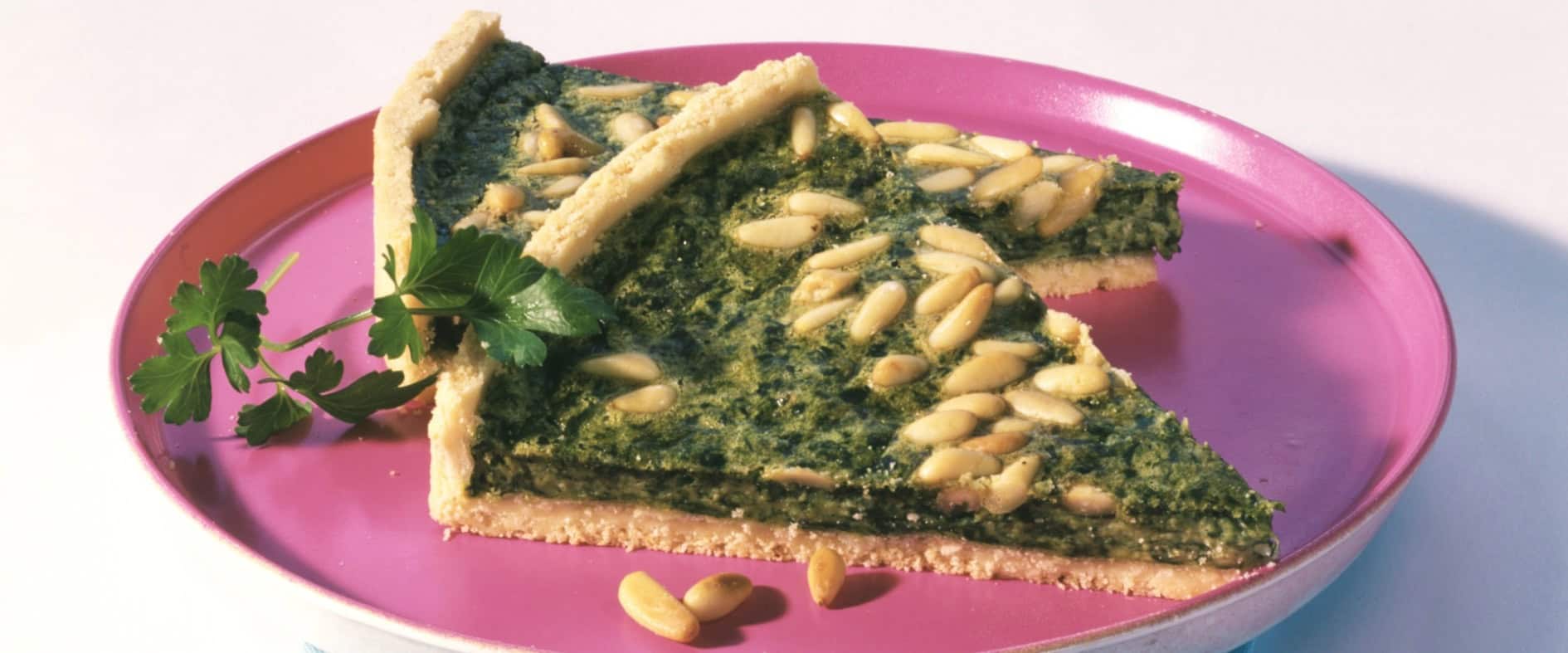 Zwei Stücke Spinatquiche mit Pinienkernen auf knusprigem Mürbeteig, serviert auf einem Teller und mit Petersilie garniert.