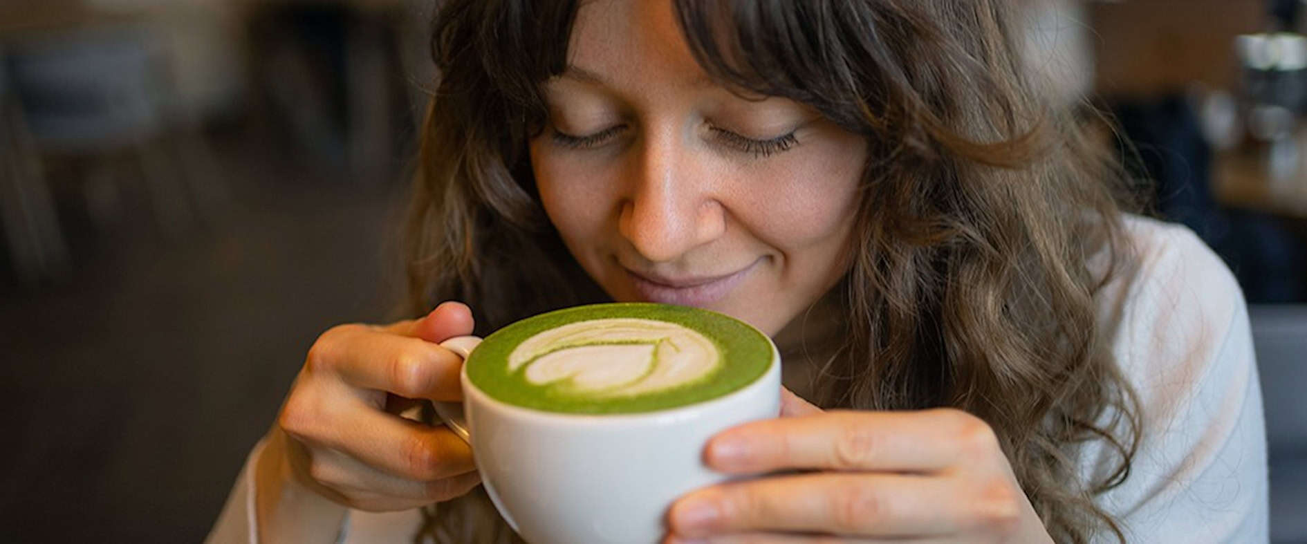 Frau genießt einen Matcha Latte mit Latte Art in einem Café als kleinen Alltagsluxus
