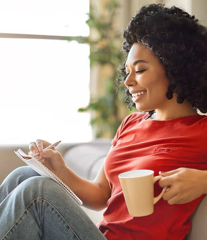 Person notiert Zahlen auf einem Block und hält eine Tasse, als Symbol für die Auswahl von Glückszahlen beim Eurojackpot