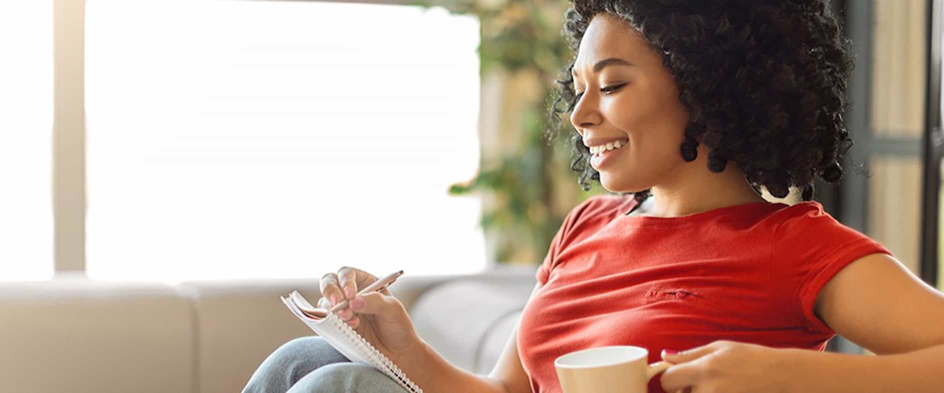 Person notiert Zahlen auf einem Block und hält eine Tasse, als Symbol für die Auswahl von Glückszahlen beim Eurojackpot