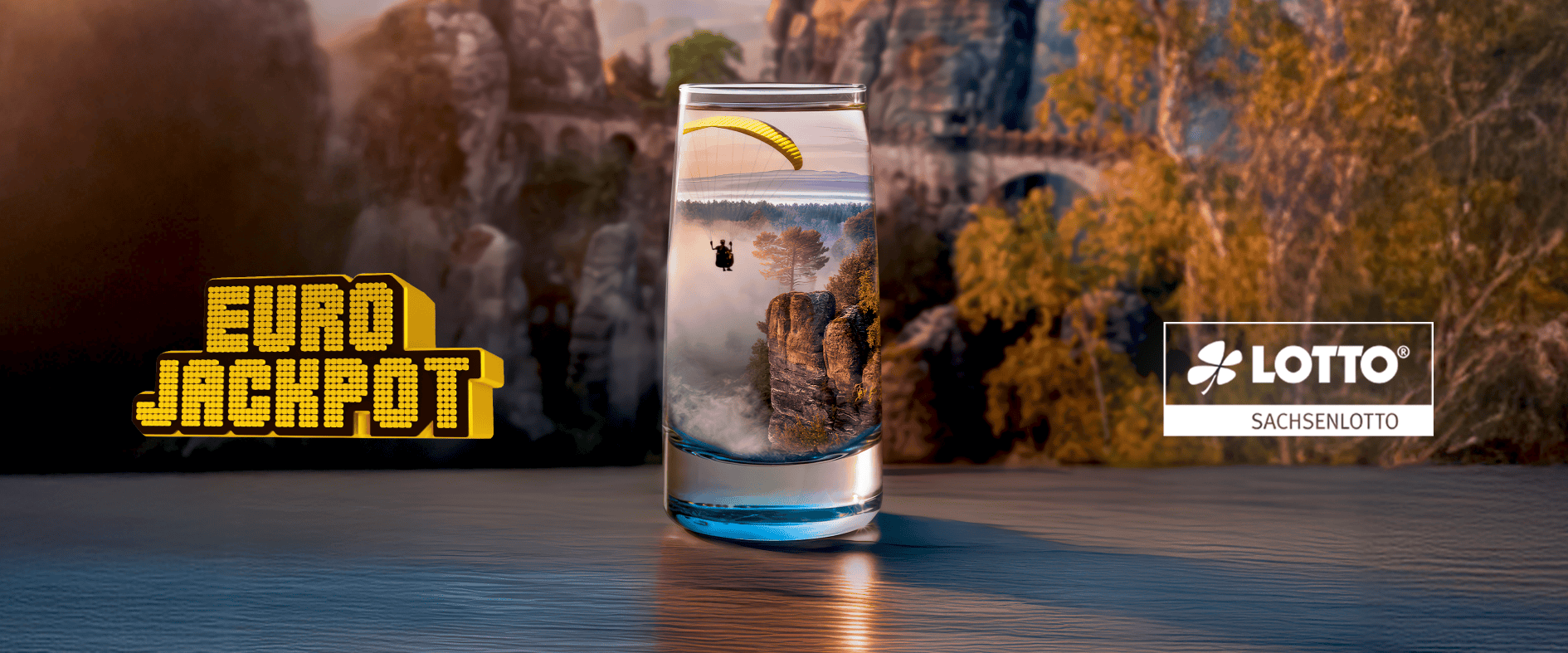 Eurojackpot Motiv von Sachsenlotto: Ein Gleitschirmflieger schwebt über einer Felsenlandschaft, gespiegelt in einem Glas vor der Sächsischen Schweiz.