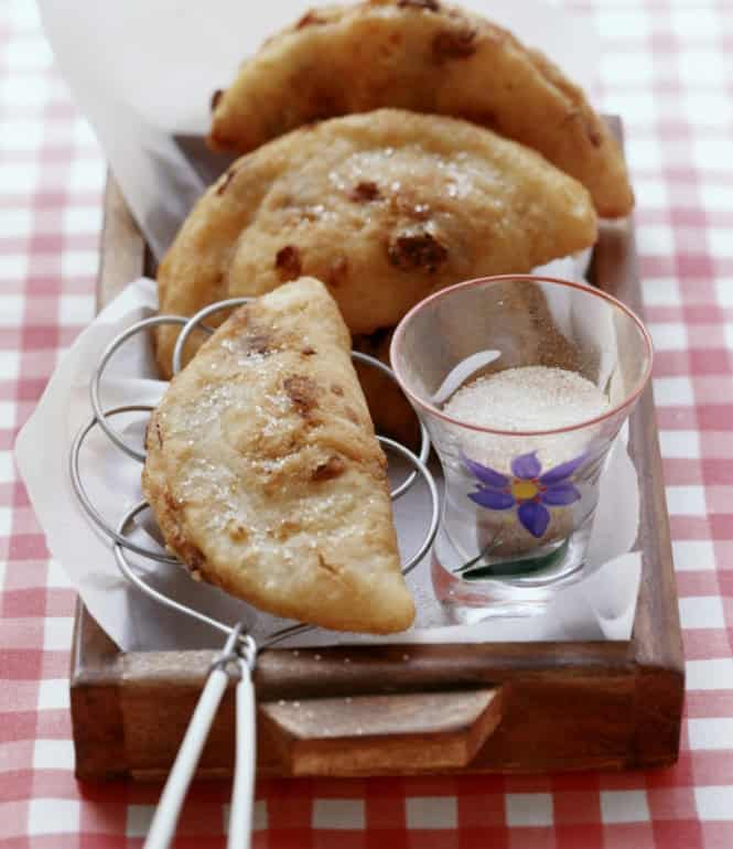 Goldbraun ausgebackene Fastnachts-Krapfen mit Trockenfruchtfüllung und Zimtzucker auf einem Holztablett.