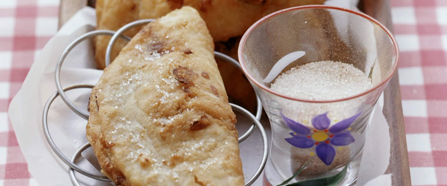 Goldbraun ausgebackene Fastnachts-Krapfen mit Trockenfruchtfüllung und Zimtzucker auf einem Holztablett.