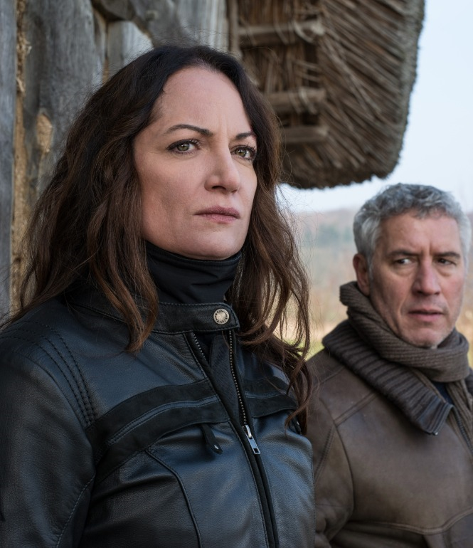 Natalia Wörner als Kriminalrätin Jana Winter vor einer Holzhütte, neben ihr ein Kollege, beide blicken angespannt in die Ferne