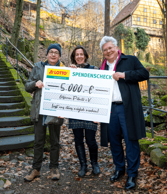 Tom Pauls, Annegret Grütze und Frank Schwarz stehen am gesperrten Keppgrund Wanderweg in Dresden und halten einen 5.000-Euro-Spendenscheck der Sachsenlotto Möglichmacher.