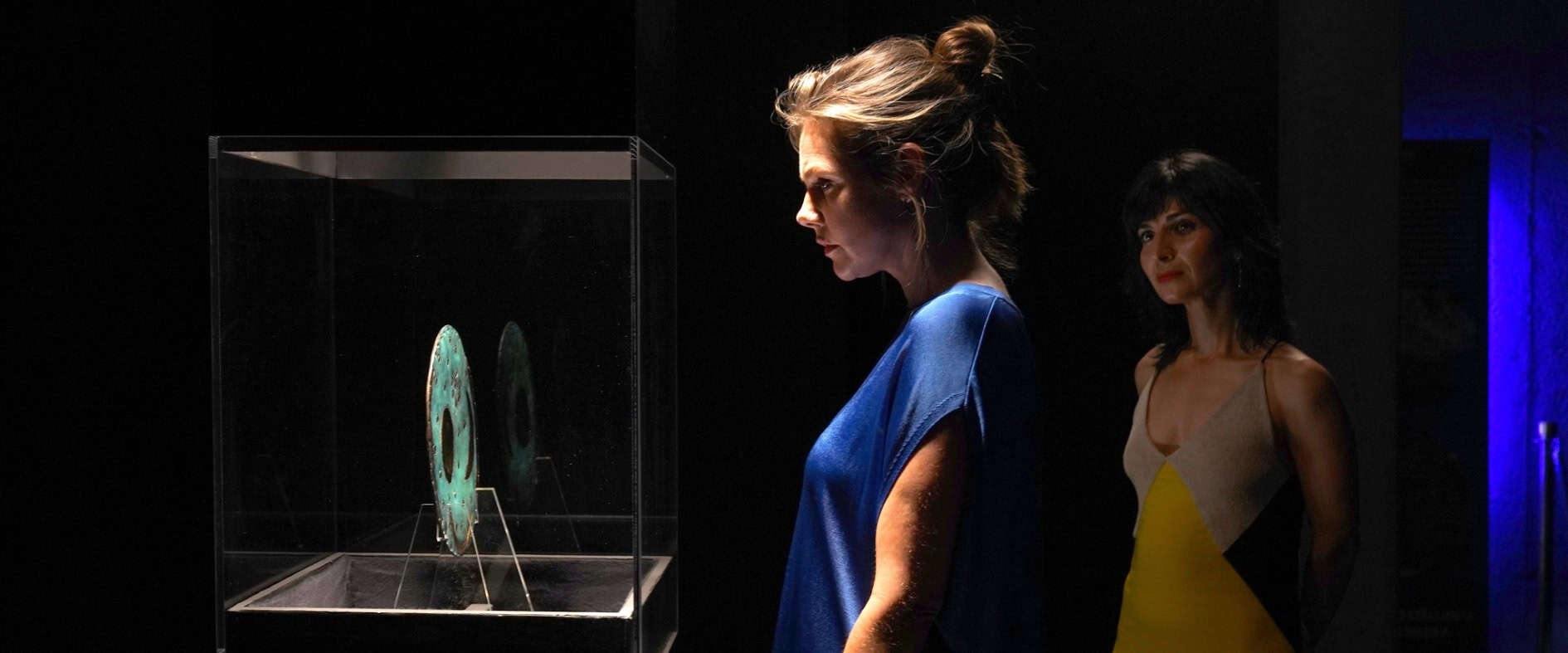Zwei Schauspielerinnen betrachten in einer dunklen Ausstellung die Himmelsscheibe von Nebra – Szene aus dem TV-Thriller ‚Das dunkle Vermächtnis‘.