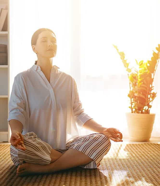Frau meditiert entspannt im Sonnenlicht zu Hause, symbolisiert Achtsamkeit und Selbstoptimierung am Morgen