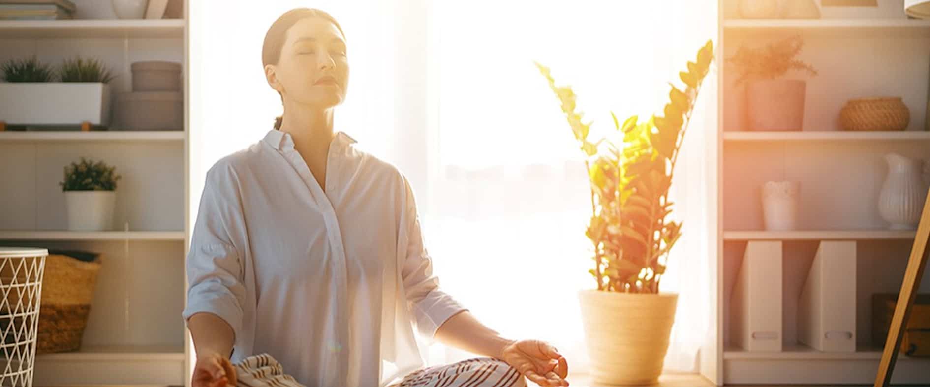Frau meditiert entspannt im Sonnenlicht zu Hause, symbolisiert Achtsamkeit und Selbstoptimierung am Morgen