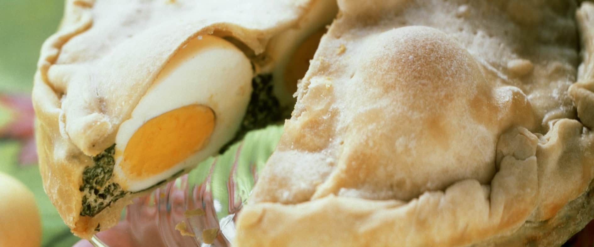 Spinat-Eier-Torte mit hart gekochten Eiern in der Füllung, geschnitten und auf einem Teller serviert, umgeben von bunt bemalten Ostereiern.