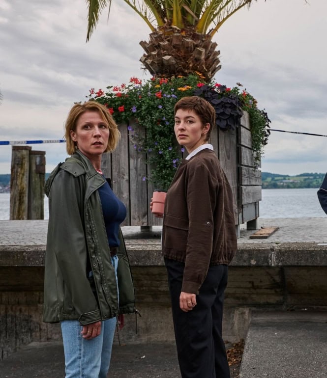 Vier Ermittler aus der ZDF-Krimiserie „Mordufer“ am Bodensee: Zwei Kommissarinnen und zwei Zollbeamte stehen und sitzen konzentriert an einem Tatort mit Blick auf den See und Palmen im Hintergrund.