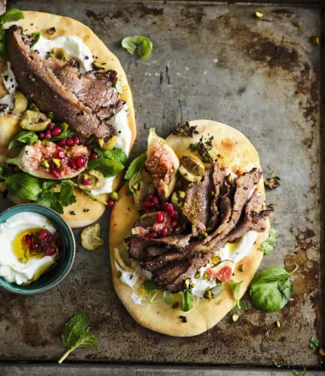 Shawarma-Fladenbrote mit zarten Rindfleischscheiben, Schafsjoghurt, Feigen, Granatapfelkernen, Pistazien und frischen Kräutern auf einem Backblech.