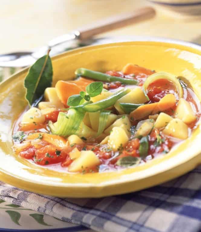 Provenzalischer Gemüseeintopf in einer gelben Schüssel, serviert mit Möhren, Kartoffeln, Lauch und einer würzigen Tomaten-Kräutersauce, garniert mit frischem Basilikum.