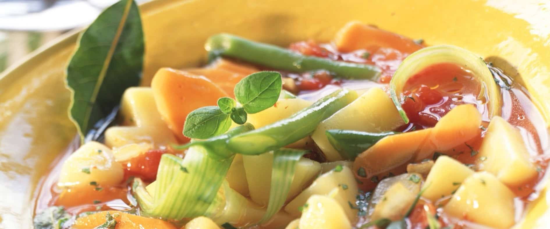 Provenzalischer Gemüseeintopf in einer gelben Schüssel, serviert mit Möhren, Kartoffeln, Lauch und einer würzigen Tomaten-Kräutersauce, garniert mit frischem Basilikum.