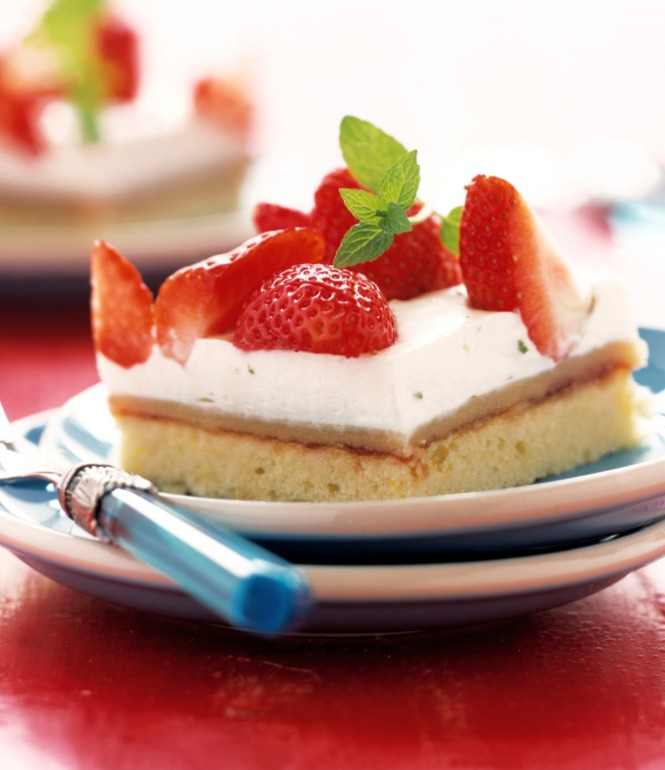 Stück Erdbeer-Schmandkuchen mit frischen Erdbeeren und Minzblatt auf einem Teller, serviert mit einer Gabel.