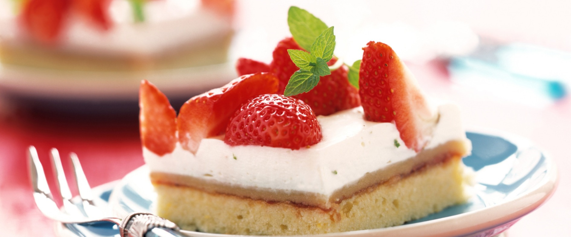 Stück Erdbeer-Schmandkuchen mit frischen Erdbeeren und Minzblatt auf einem Teller, serviert mit einer Gabel.