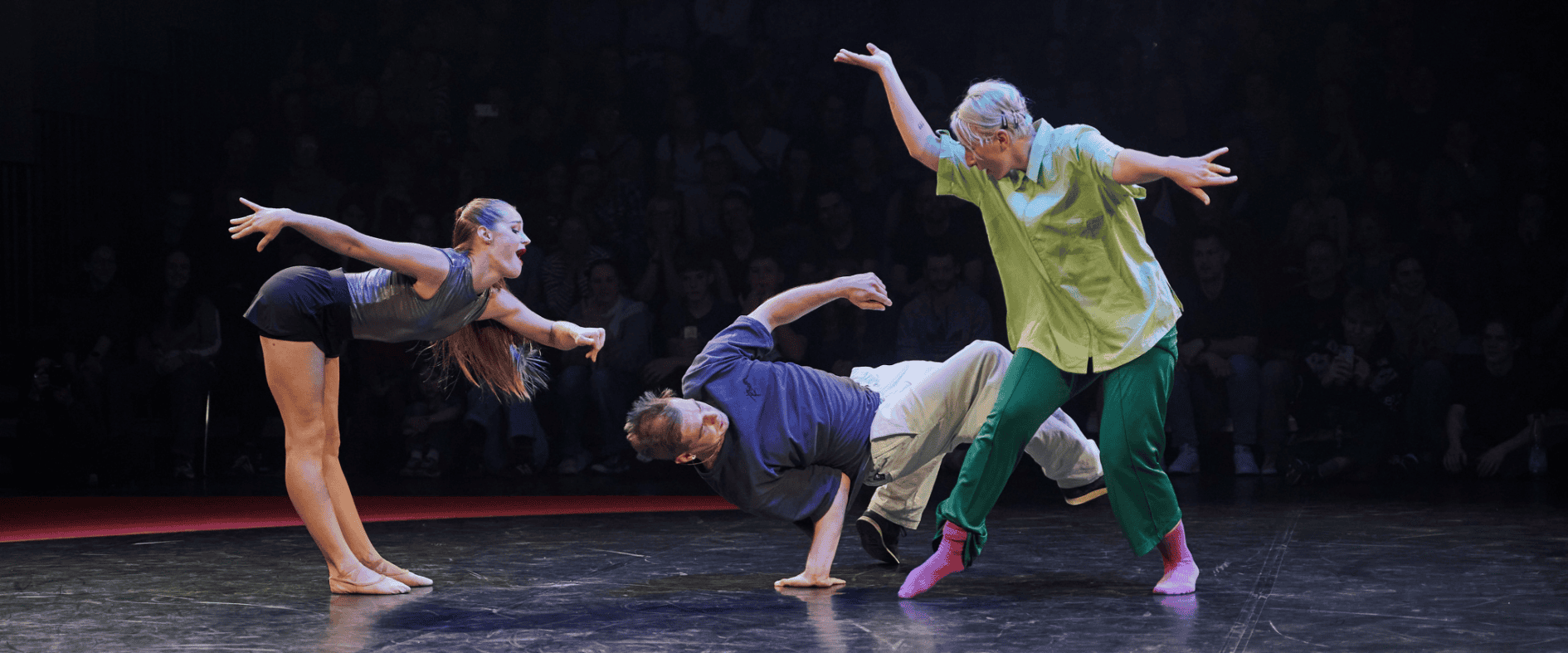 Drei Tänzer performen eine zeitgenössische Tanzszene auf der Bühne vor Publikum