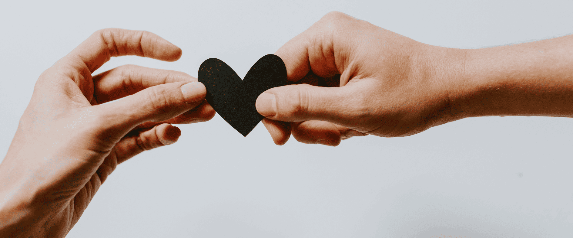 Hände halten ein schwarzes Herz aus Papier als Symbol für Verbundenheit