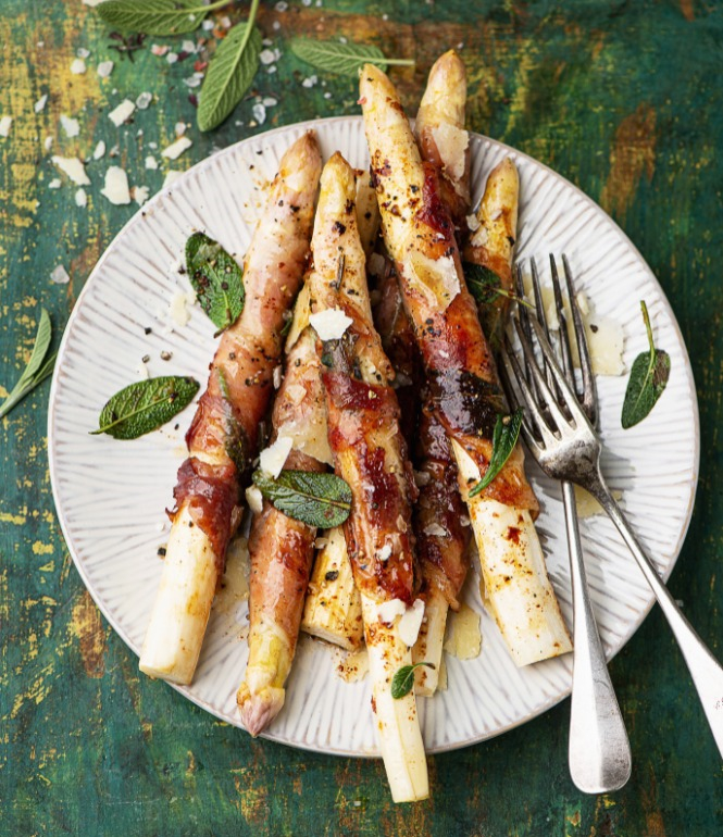 Saltimbocca vom weißen Spargel mit Prosciutto und Salbei auf einem Teller, garniert mit Parmesan und Salbeiblättern.